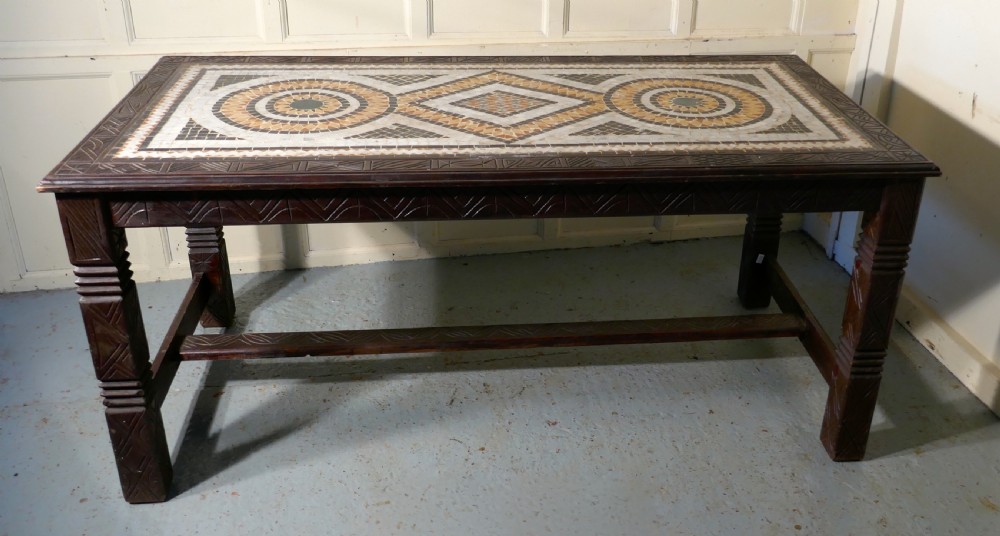 A rectangular dark wood dining table featuring a detailed geometric stone mosaic top, hand-carved geometric patterns on the apron, and carved legs connected by stretchers. View III