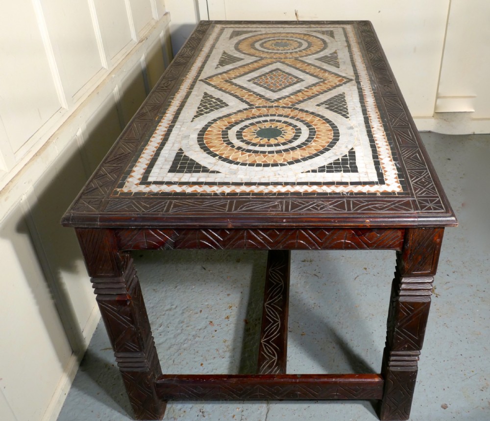 A rectangular dark wood dining table featuring a detailed geometric stone mosaic top, hand-carved geometric patterns on the apron, and carved legs connected by stretchers. View V