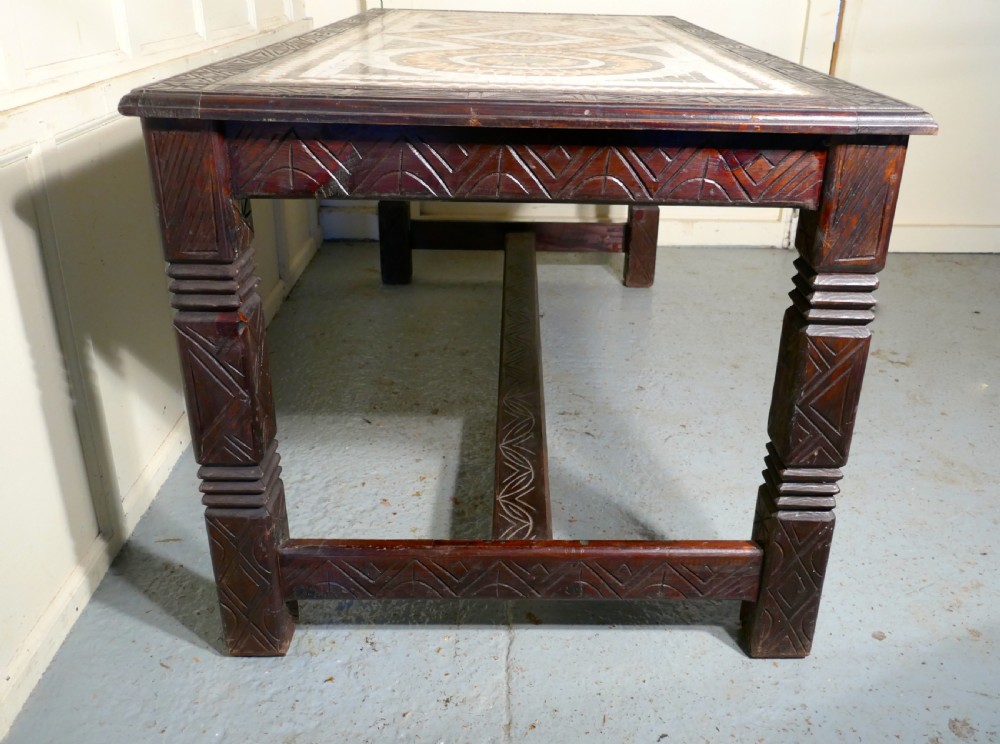 A rectangular dark wood dining table featuring a detailed geometric stone mosaic top, hand-carved geometric patterns on the apron, and carved legs connected by stretchers. View VIII