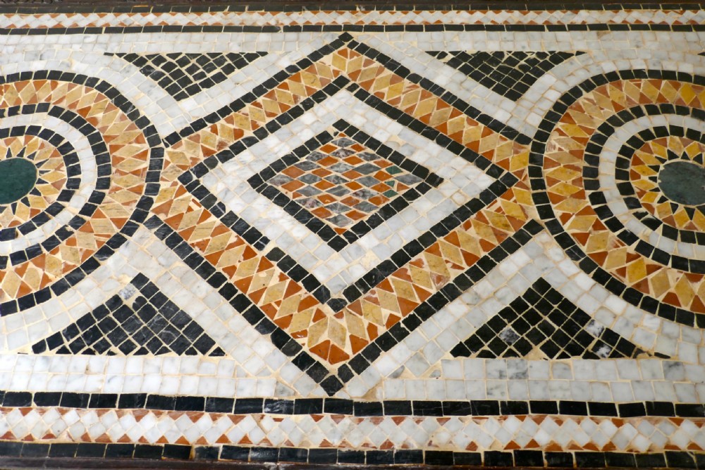 A rectangular dark wood dining table featuring a detailed geometric stone mosaic top, hand-carved geometric patterns on the apron, and carved legs connected by stretchers. View IX