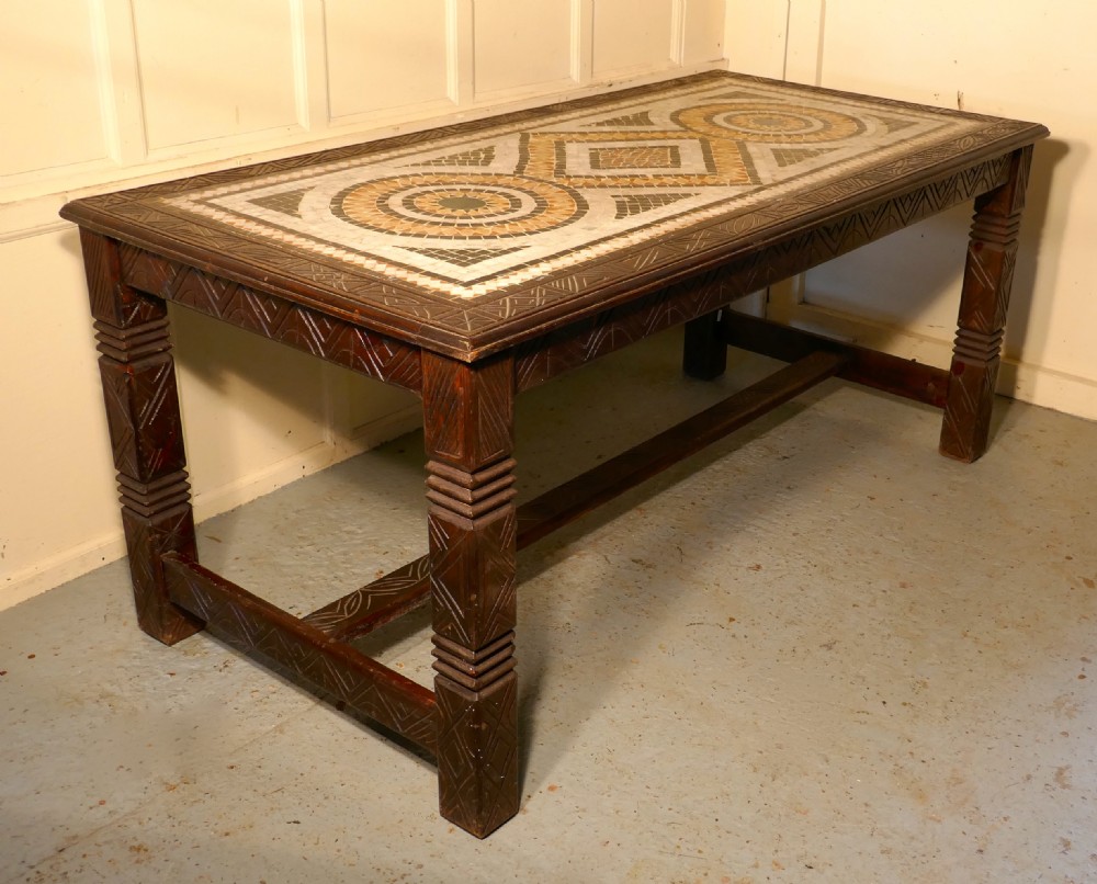 A rectangular dark wood dining table featuring a detailed geometric stone mosaic top, hand-carved geometric patterns on the apron, and carved legs connected by stretchers. View XI