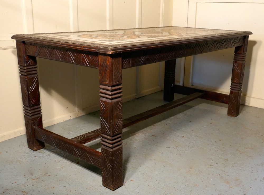 A rectangular dark wood dining table featuring a detailed geometric stone mosaic top, hand-carved geometric patterns on the apron, and carved legs connected by stretchers. View XII