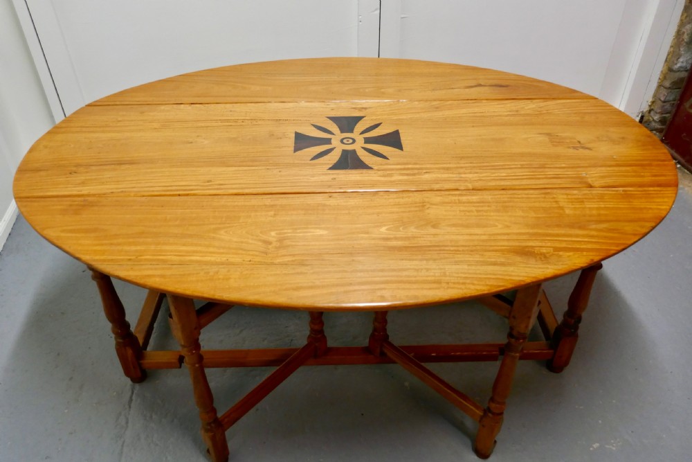 An oval wooden gateleg dining table featuring a central geometric star inlay, turned legs, and foldable drop leaves.