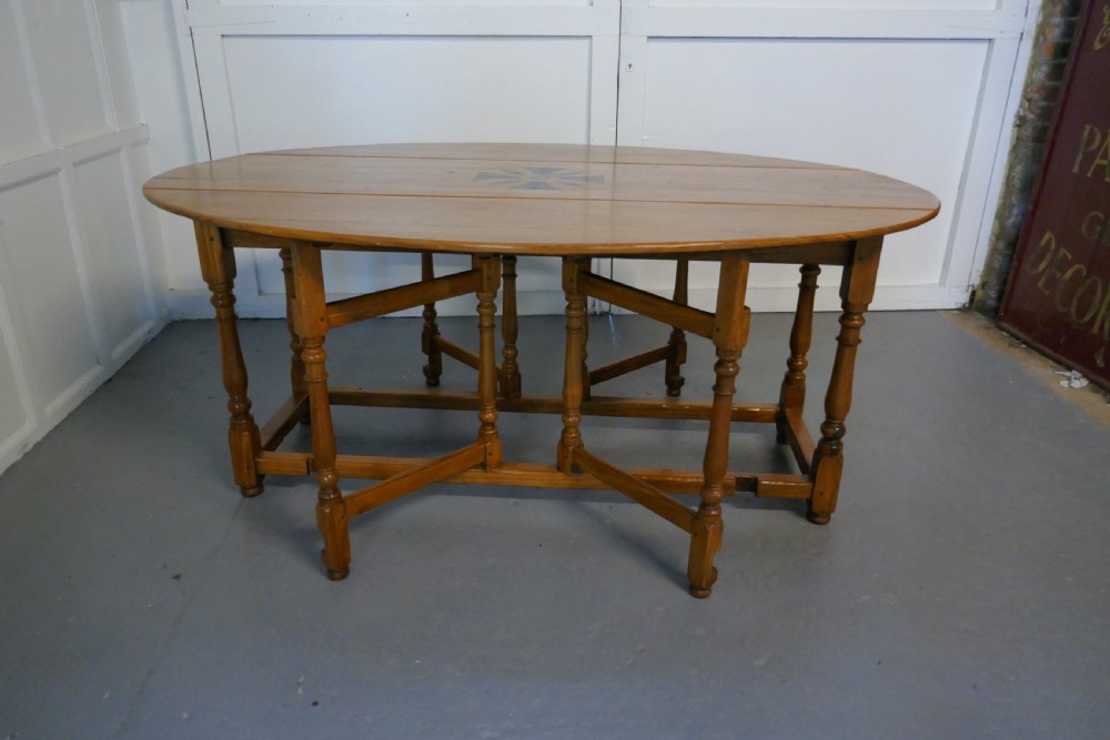 An oval wooden gateleg dining table featuring a central geometric star inlay, turned legs, and foldable drop leaves. View V