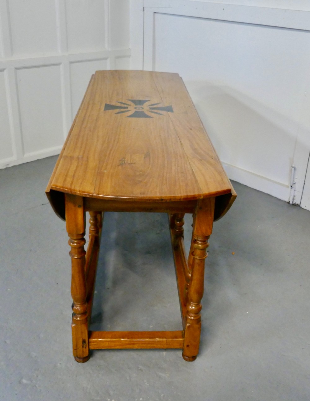 An oval wooden gateleg dining table featuring a central geometric star inlay, turned legs, and foldable drop leaves. View VI