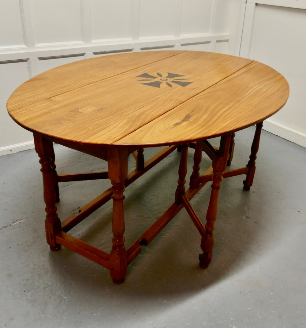 An oval wooden gateleg dining table featuring a central geometric star inlay, turned legs, and foldable drop leaves. View VII