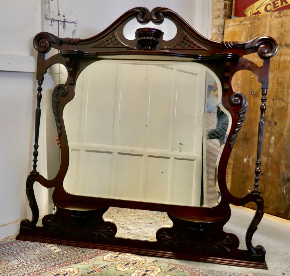 A large carved mahogany overmantel mirror in the Chinese Chippendale style, featuring pierced fretwork, turned side supports, side display shelves, and a shaped glass plate.