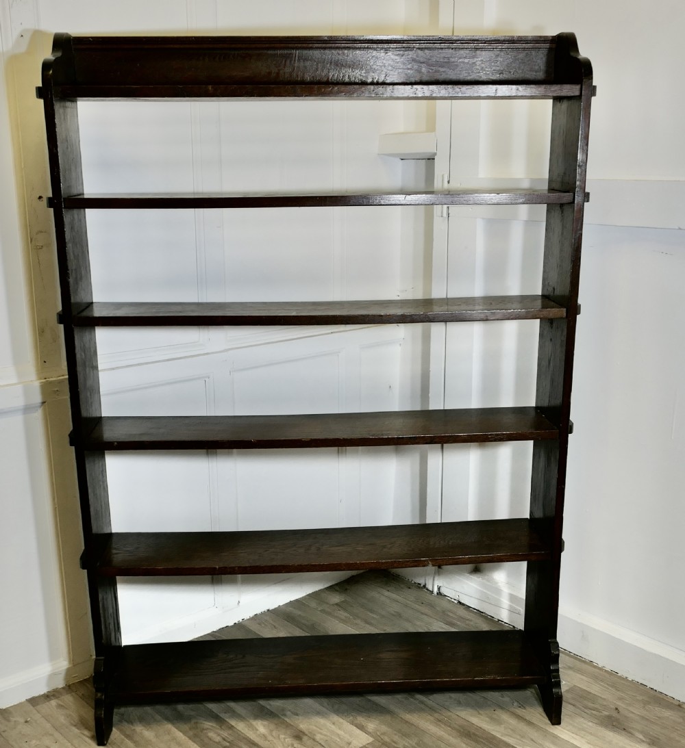 A tall open-front Arts and Crafts dark oak bookcase with six horizontal shelves and shaped side gallery rails.