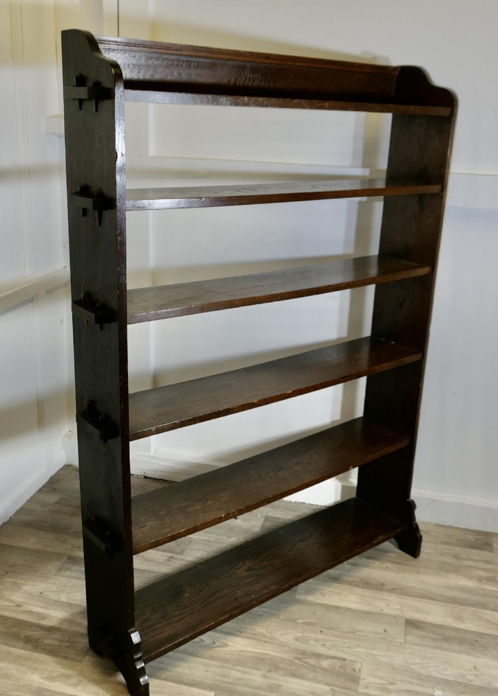 A tall open-front Arts and Crafts dark oak bookcase with six horizontal shelves and shaped side gallery rails. View VII