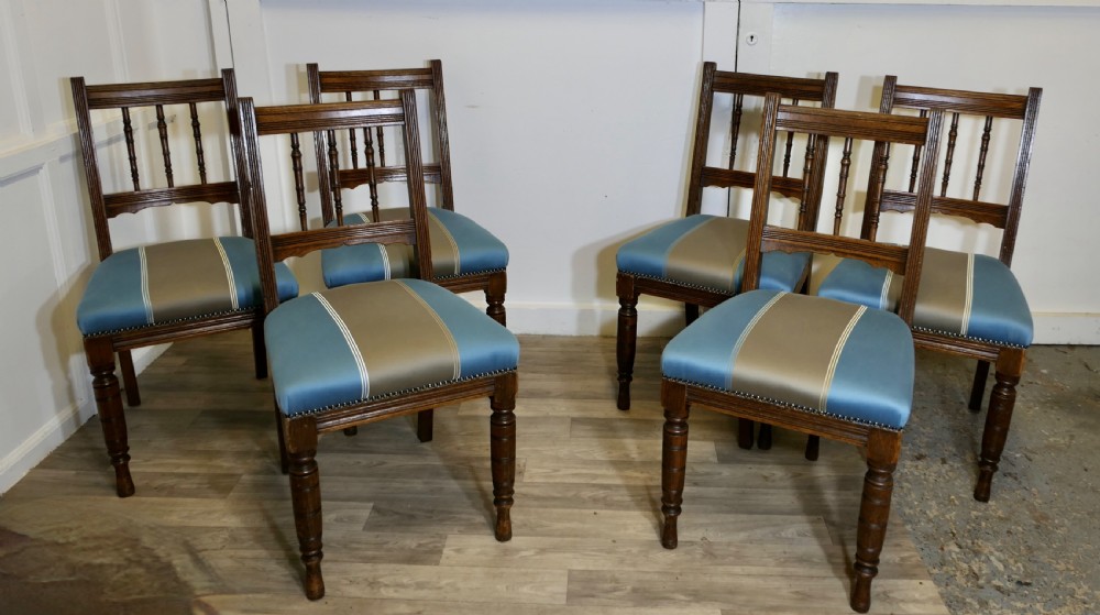 A set of six Edwardian oak dining chairs featuring turned front legs, vertical back spindles, and blue and grey striped satin seats with stud detail.