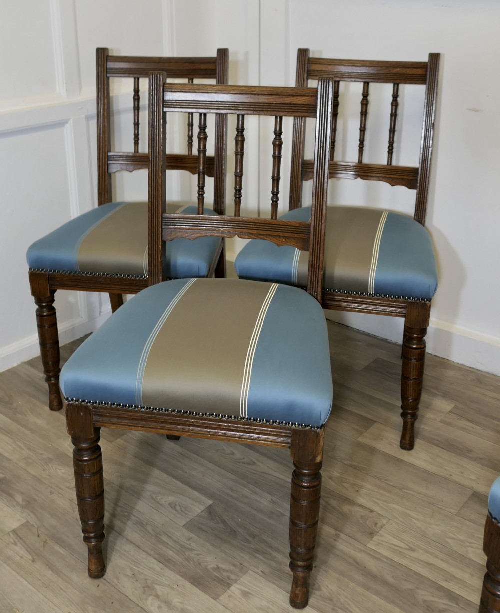 A set of six Edwardian oak dining chairs featuring turned front legs, vertical back spindles, and blue and grey striped satin seats with stud detail. View V
