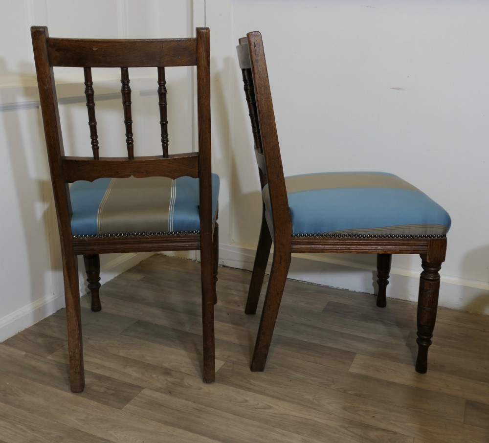 A set of six Edwardian oak dining chairs featuring turned front legs, vertical back spindles, and blue and grey striped satin seats with stud detail. View X