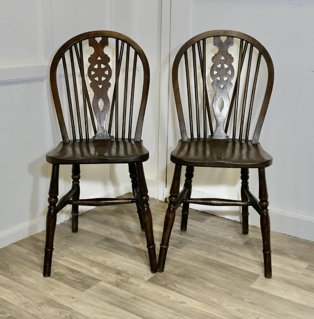 A pair of dark brown Victorian beech and elm chairs featuring wheelback pierced splats, turned legs, and contoured wooden seats.