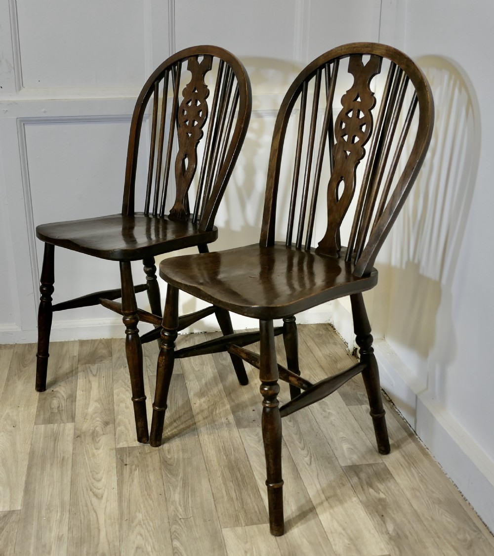 A pair of dark brown Victorian beech and elm chairs featuring wheelback pierced splats, turned legs, and contoured wooden seats. View III