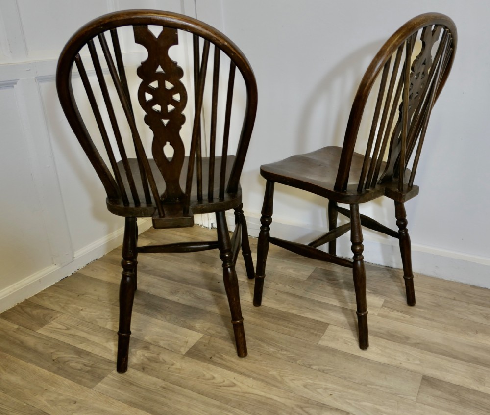 A pair of dark brown Victorian beech and elm chairs featuring wheelback pierced splats, turned legs, and contoured wooden seats. View V