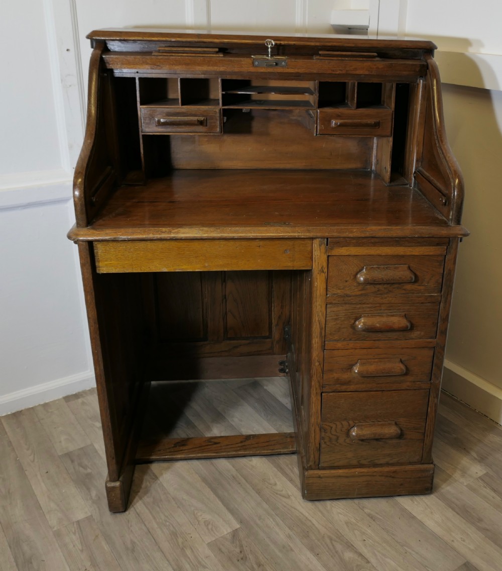 An Art Deco oak roll top desk featuring a flexible tambour shutter, fitted internal cubbies, and a single pedestal with four stacked drawers.