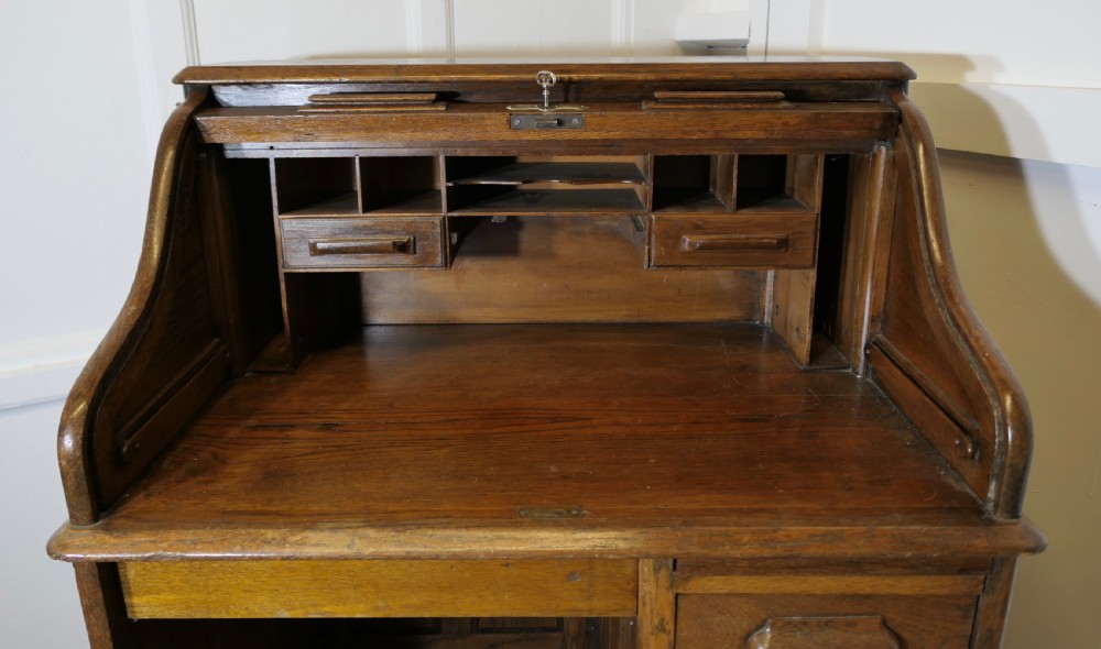 An Art Deco oak roll top desk featuring a flexible tambour shutter, fitted internal cubbies, and a single pedestal with four stacked drawers. View II