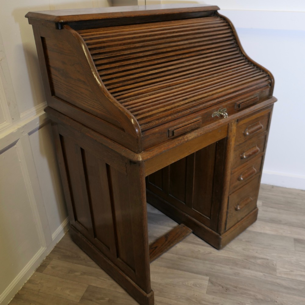 An Art Deco oak roll top desk featuring a flexible tambour shutter, fitted internal cubbies, and a single pedestal with four stacked drawers. View V