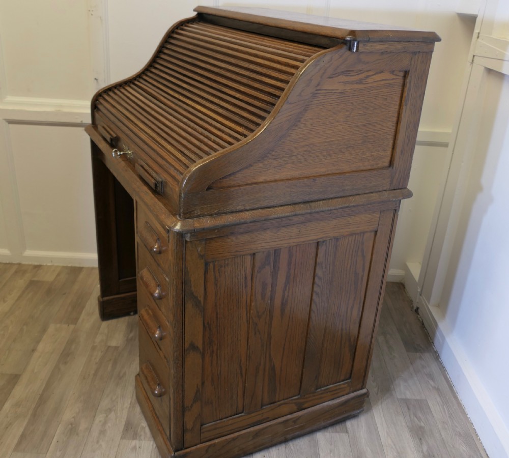An Art Deco oak roll top desk featuring a flexible tambour shutter, fitted internal cubbies, and a single pedestal with four stacked drawers. View VI