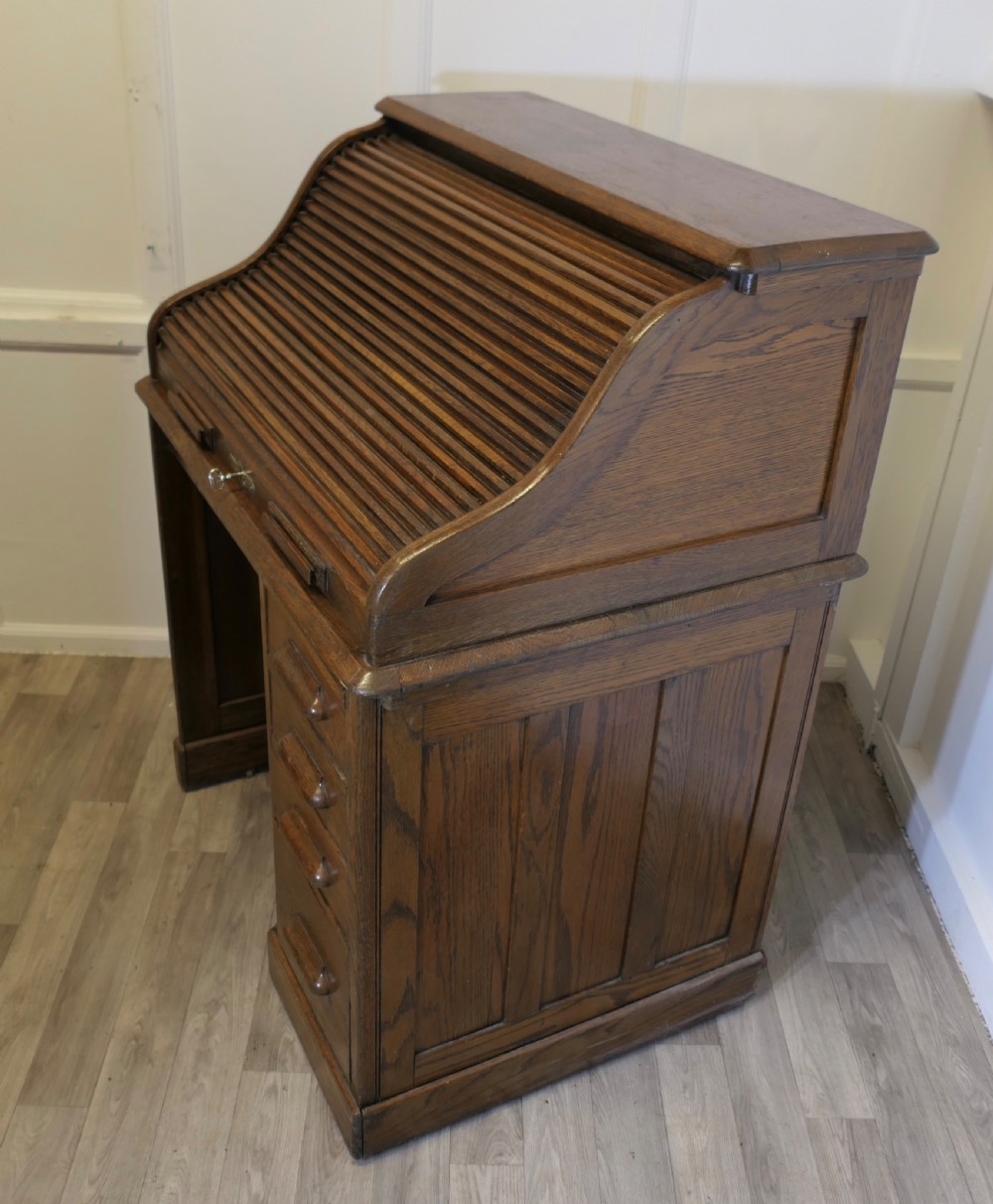 An Art Deco oak roll top desk featuring a flexible tambour shutter, fitted internal cubbies, and a single pedestal with four stacked drawers. View VII
