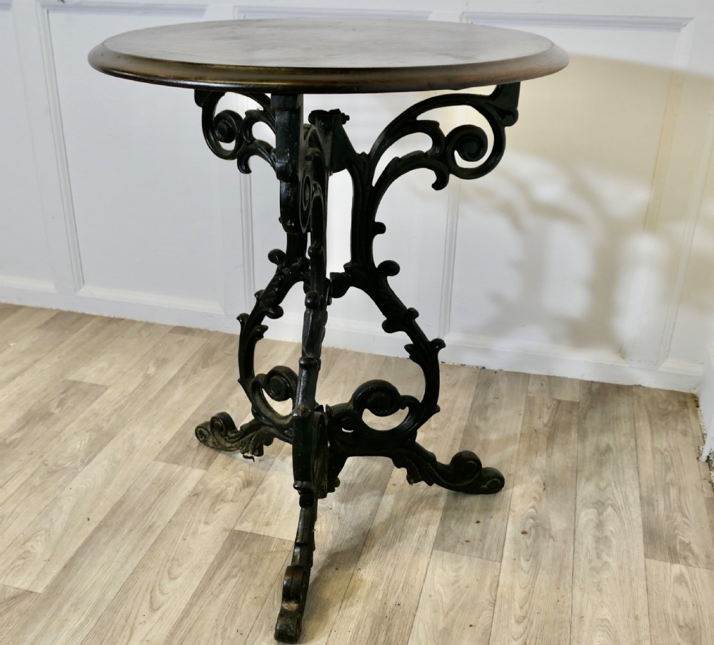 A Victorian occasional table with a dark polished circular wooden top mounted on an ornate black cast iron tripod scrollwork base. View V