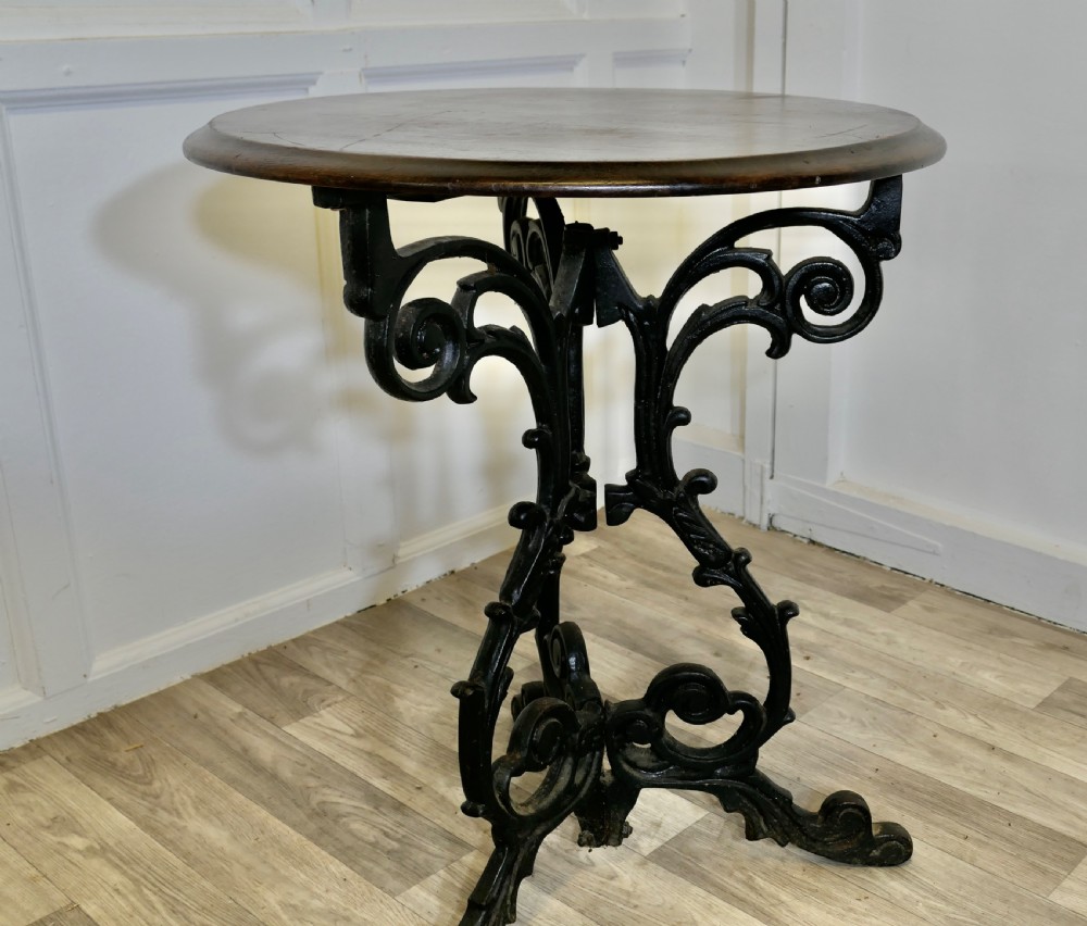 A Victorian occasional table with a dark polished circular wooden top mounted on an ornate black cast iron tripod scrollwork base. View VI