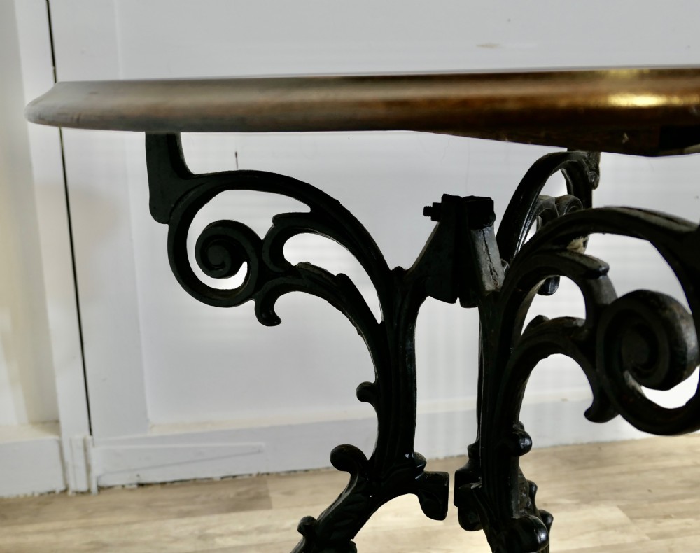 A Victorian occasional table with a dark polished circular wooden top mounted on an ornate black cast iron tripod scrollwork base. View VII