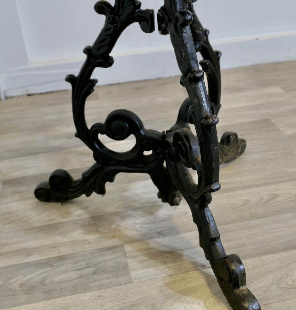 A Victorian occasional table with a dark polished circular wooden top mounted on an ornate black cast iron tripod scrollwork base. View VIII