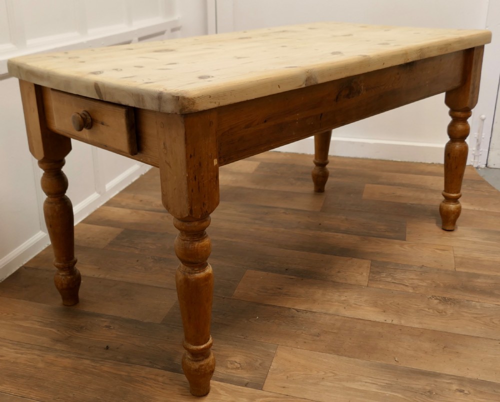 A rectangular pine kitchen table with a scrubbed natural wood top, turned legs, and a single drawer with a wooden knob pull.