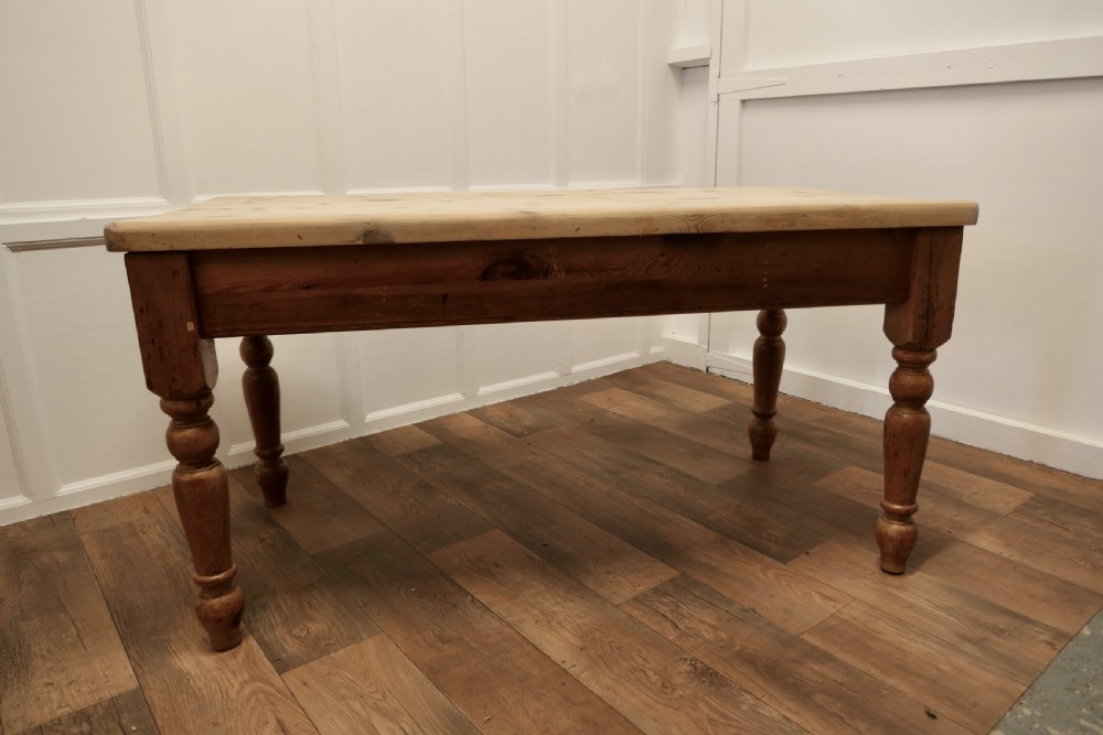 A rectangular pine kitchen table with a scrubbed natural wood top, turned legs, and a single drawer with a wooden knob pull. View V
