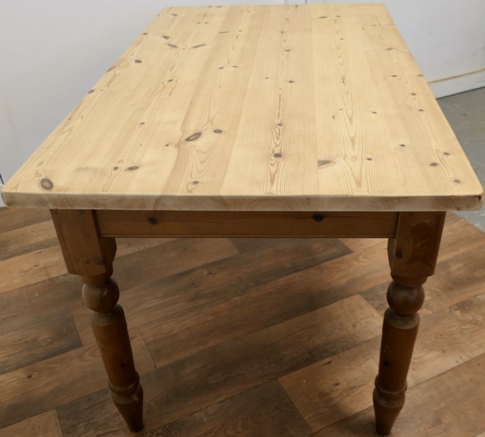 A rectangular pine kitchen table with a scrubbed natural wood top, turned legs, and a single drawer with a wooden knob pull. View VII
