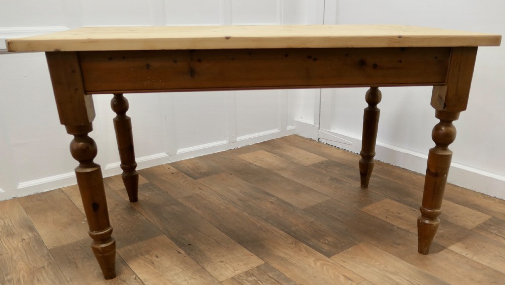 A rectangular pine kitchen table with a scrubbed natural wood top, turned legs, and a single drawer with a wooden knob pull. View X