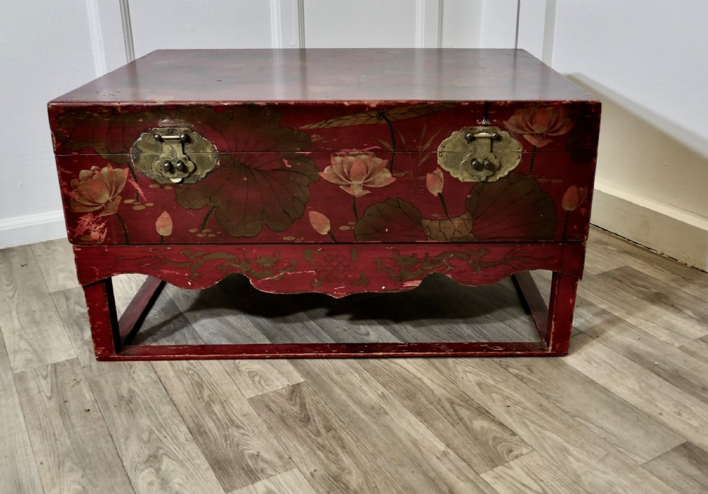 A red painted Chinoiserie marriage chest decorated with lotus motifs, raised on a low timber stand with brass clasps.