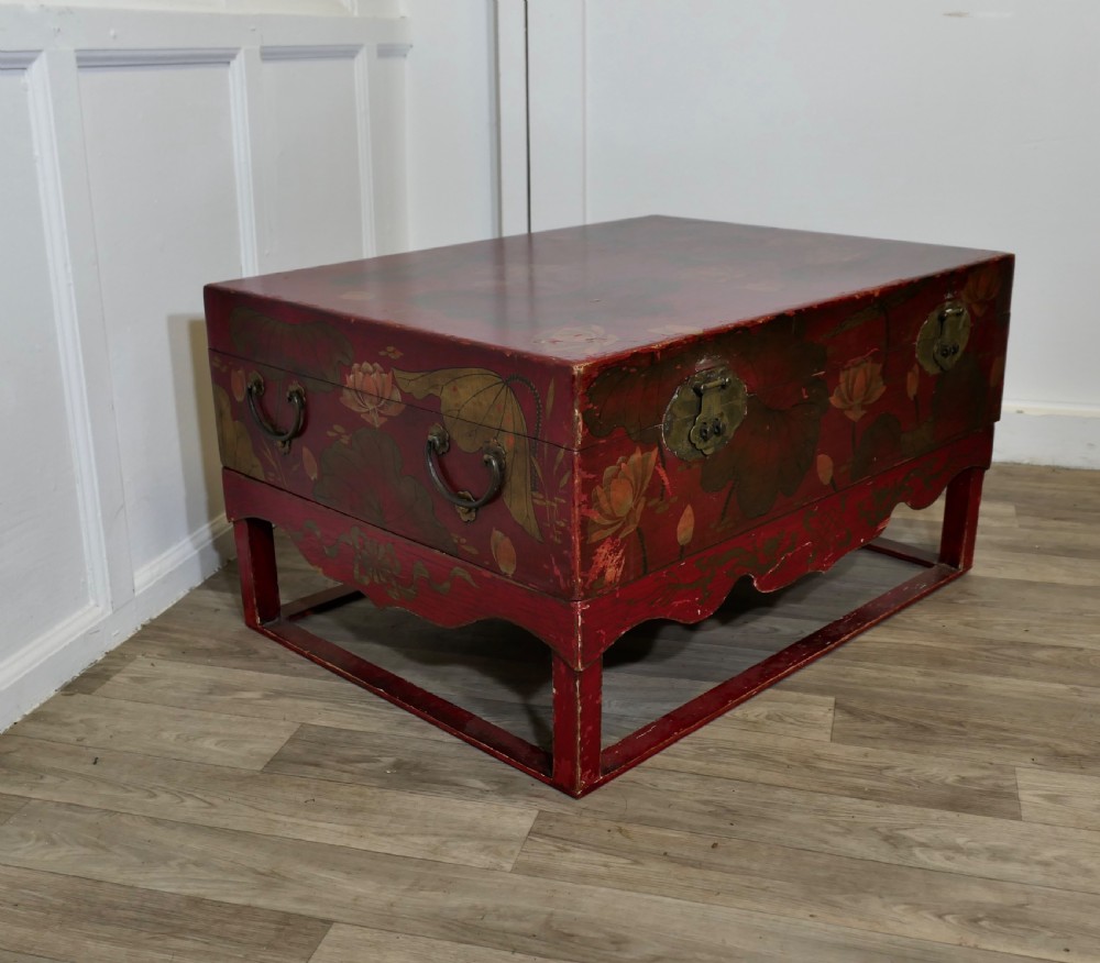 A red painted Chinoiserie marriage chest decorated with lotus motifs, raised on a low timber stand with brass clasps. View V