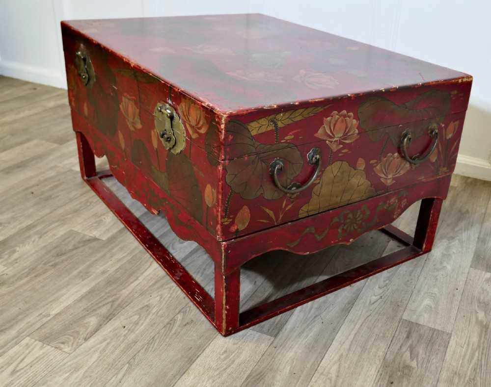 A red painted Chinoiserie marriage chest decorated with lotus motifs, raised on a low timber stand with brass clasps. View VI