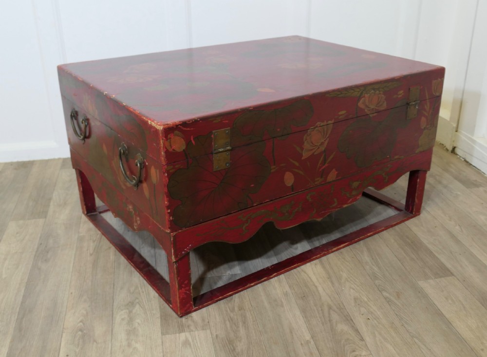 A red painted Chinoiserie marriage chest decorated with lotus motifs, raised on a low timber stand with brass clasps. View X
