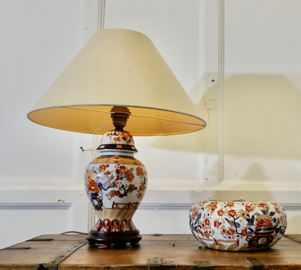 A Japanese Imari porcelain vase converted into a table lamp with a cream conical shade, positioned beside a matching decorated lidded bowl.