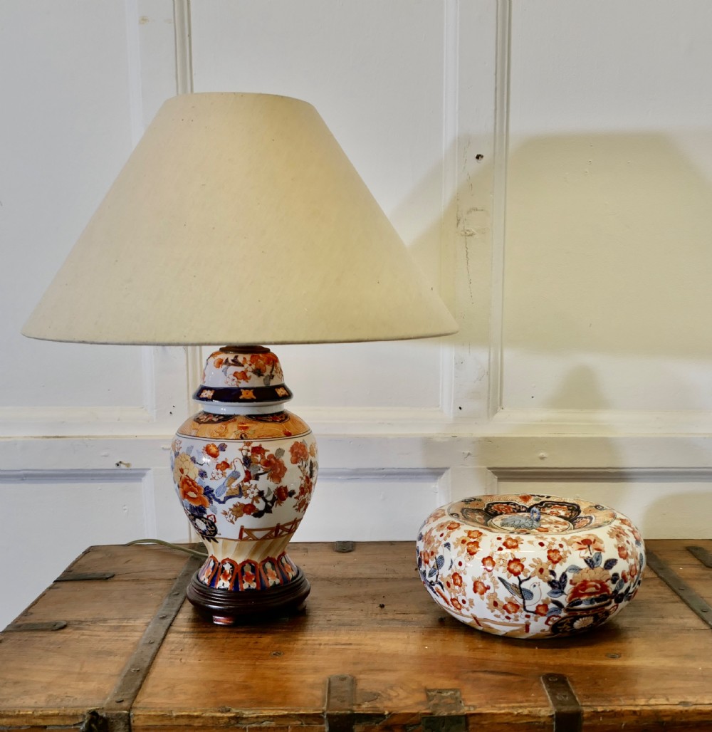 A Japanese Imari porcelain vase converted into a table lamp with a cream conical shade, positioned beside a matching decorated lidded bowl. View II