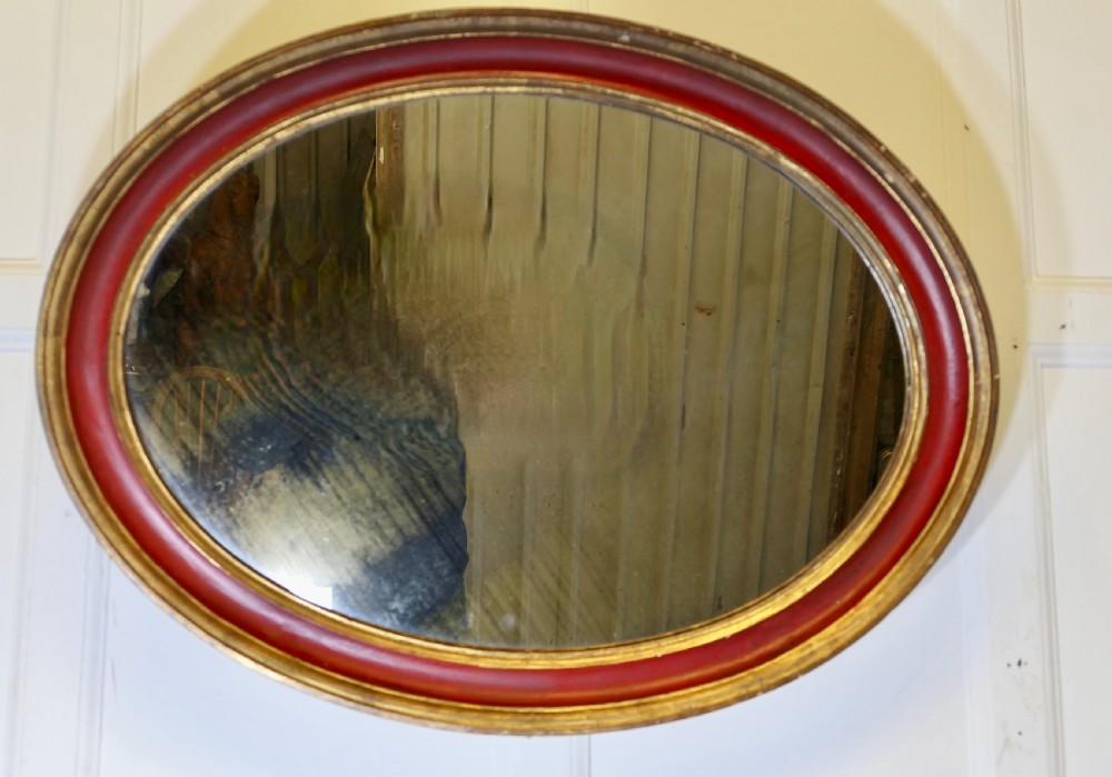 A large oval wall mirror featuring a deep red rounded moulding with gilded inner and outer borders. View II