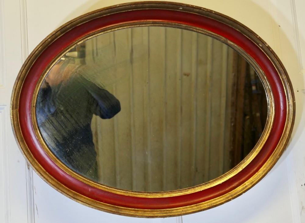 A large oval wall mirror featuring a deep red rounded moulding with gilded inner and outer borders. View III