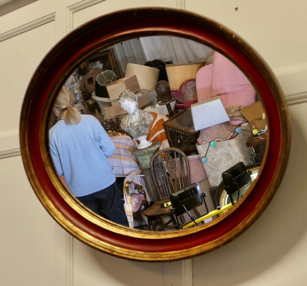 A large oval wall mirror featuring a deep red rounded moulding with gilded inner and outer borders. View IV