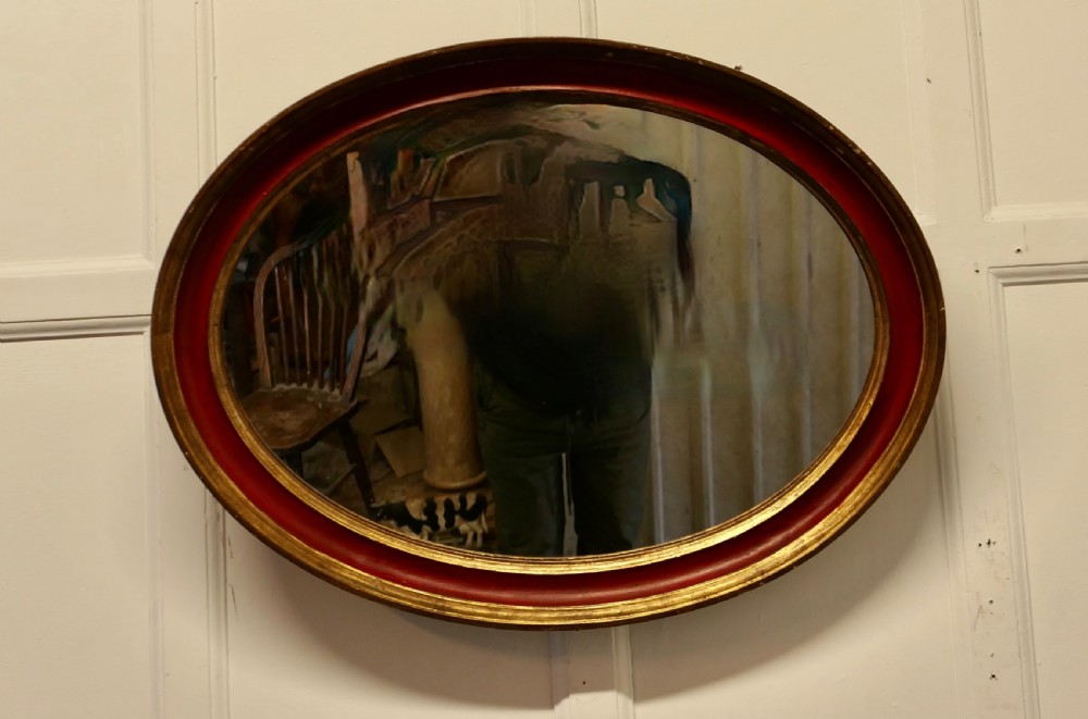 A large oval wall mirror featuring a deep red rounded moulding with gilded inner and outer borders. View VI