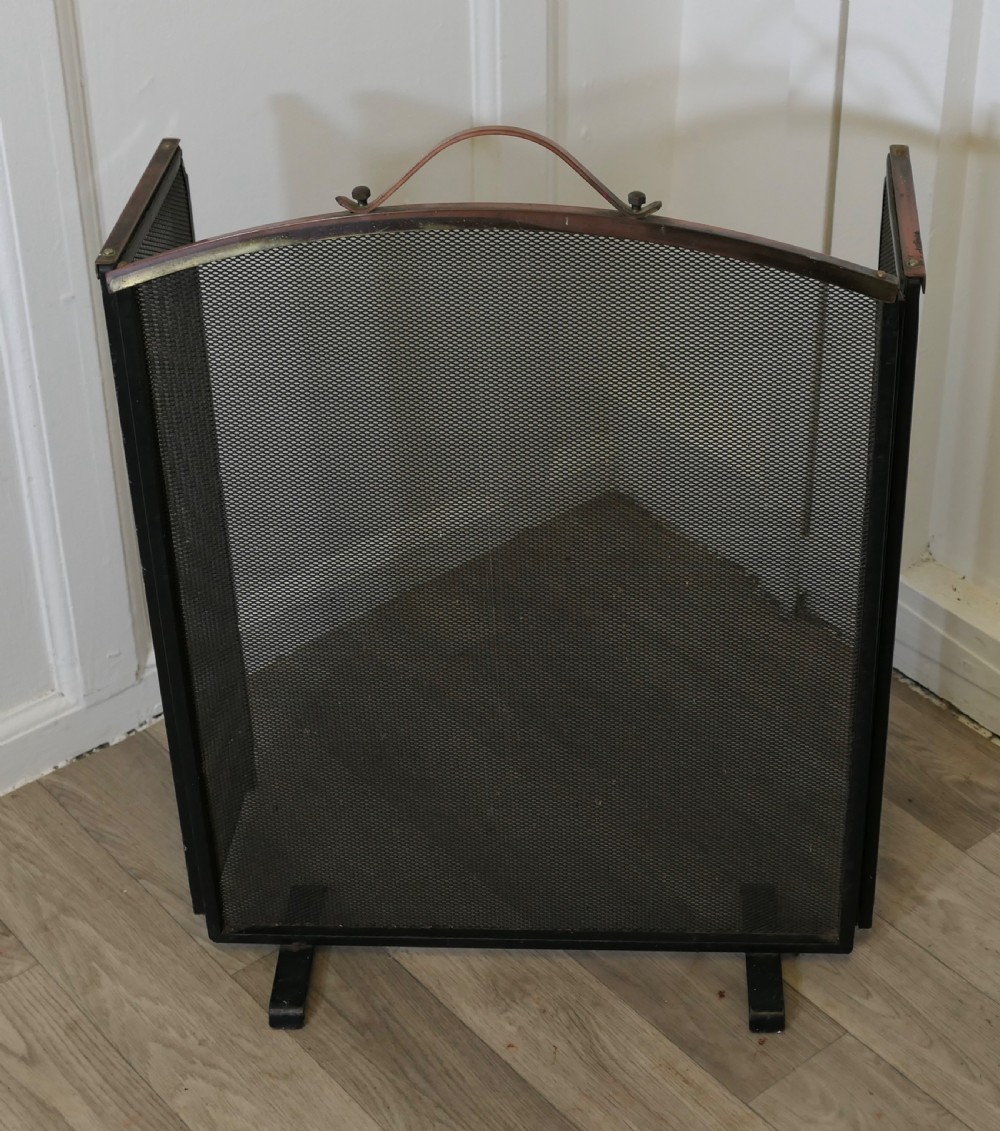A folding black metal wire mesh fire guard featuring an arched copper top rail with a central carrying handle. View II