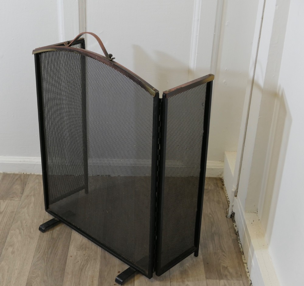 A folding black metal wire mesh fire guard featuring an arched copper top rail with a central carrying handle. View III