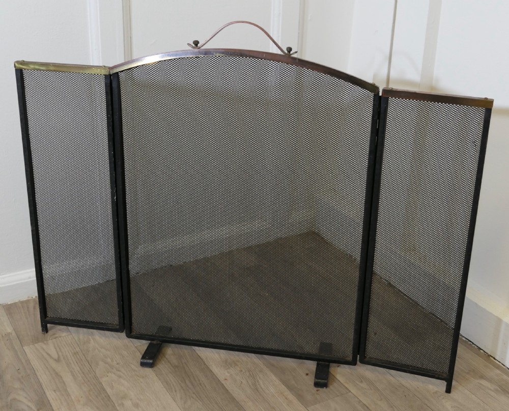 A folding black metal wire mesh fire guard featuring an arched copper top rail with a central carrying handle. View IV