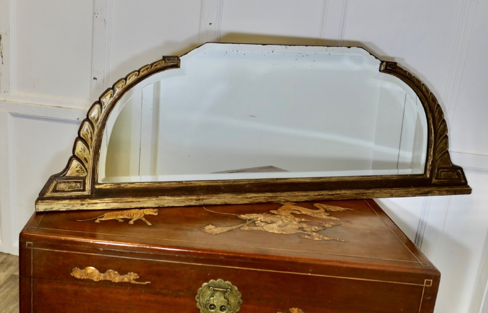 A wide Art Deco overmantel mirror featuring a low horizontal frame with dark wood moulding and gold gilded shoulders carved in a stylised leaf pattern. View V