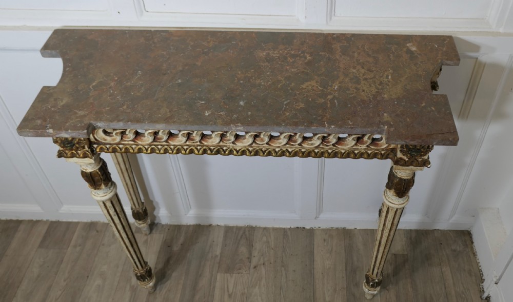 A French Neoclassical style console table featuring a grey marble top, carved pierced frieze, and cream painted tapered fluted legs with gilded accents. View II