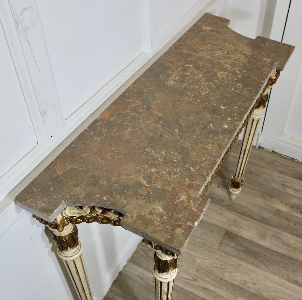A French Neoclassical style console table featuring a grey marble top, carved pierced frieze, and cream painted tapered fluted legs with gilded accents. View VII