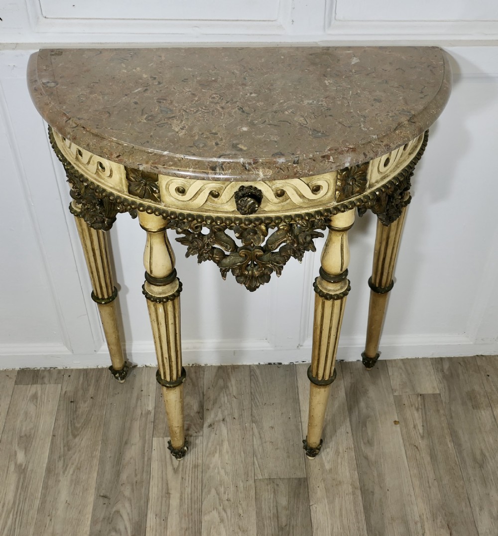 A semi-circular demilune console table featuring a marble top, a painted cream frame with gold leaf highlights, and carved fluted legs. View II
