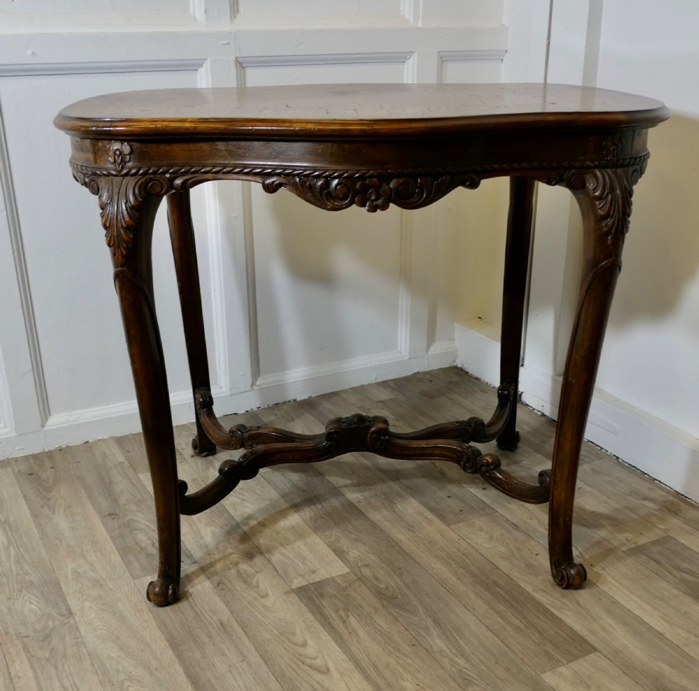 An antique carved walnut occasional table featuring a shaped serpentine top, cabriole legs, and an ornamental carved X-frame stretcher.